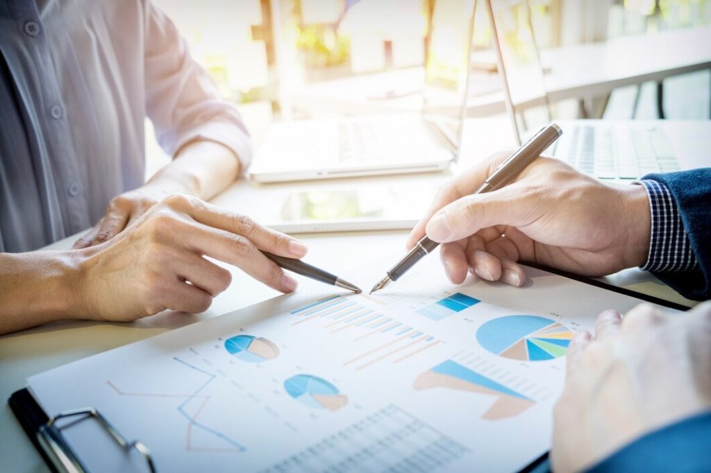 Two people discussing data and charts on a printed business report at a desk.